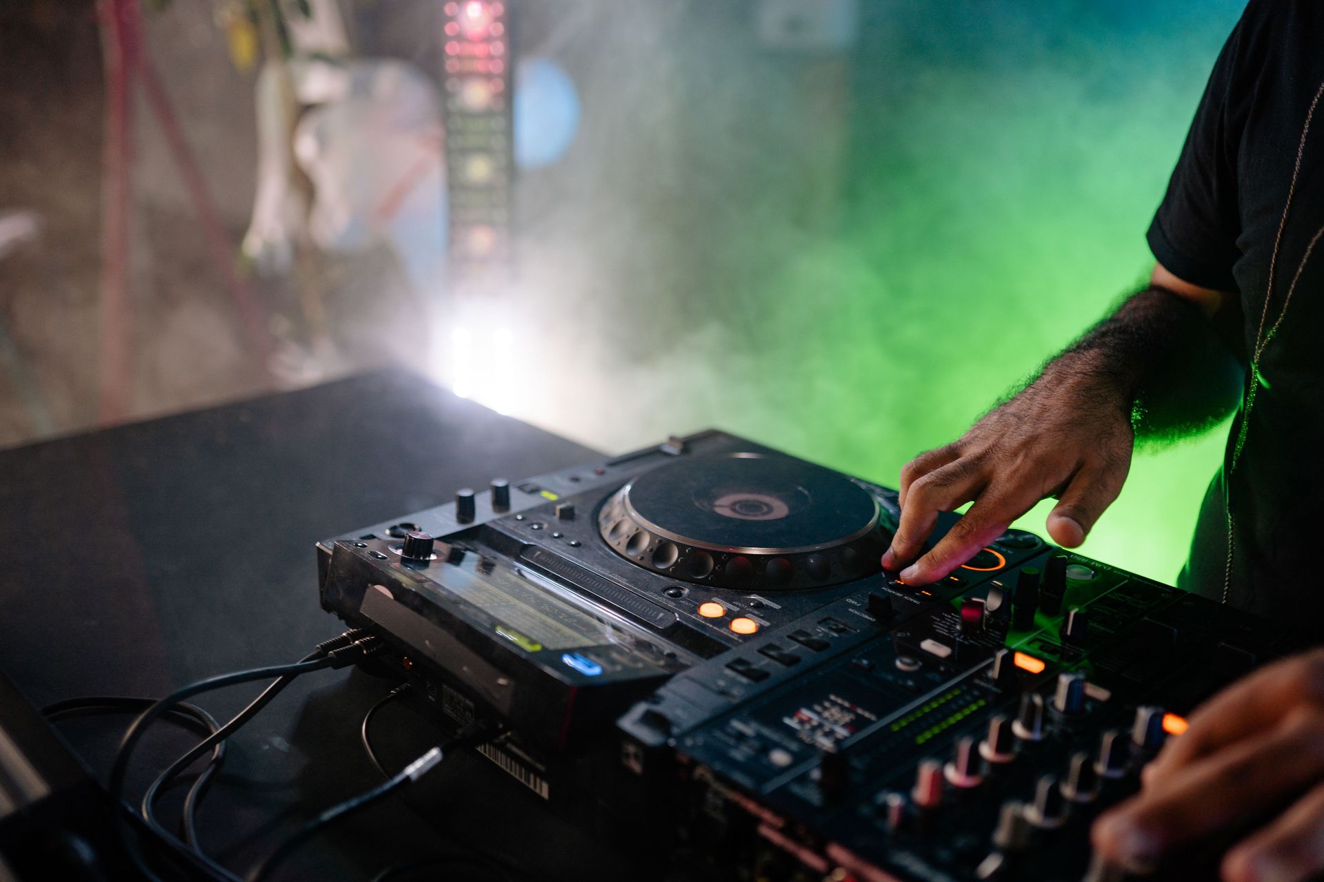 DJ playing music on turntable with vibrant lighting and smoke in a nightclub setting.